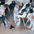 Cleans floor. Group of workers clean modern office together at daytime Cleans floor. Group of workers clean modern office together at daytime