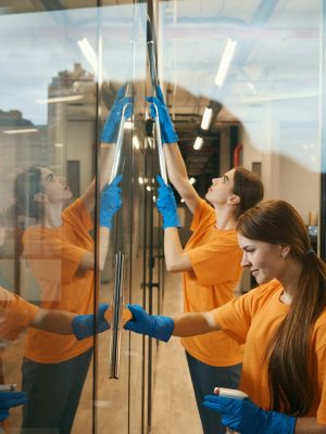 Young cleaners clean mirrored windows coworking spacer, they in simple uniforms Young cleaners clean mirrored windows coworking spacer, they in simple uniforms